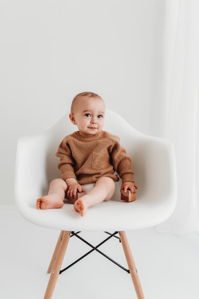 baby in a brown sweater sitting on a big white chair