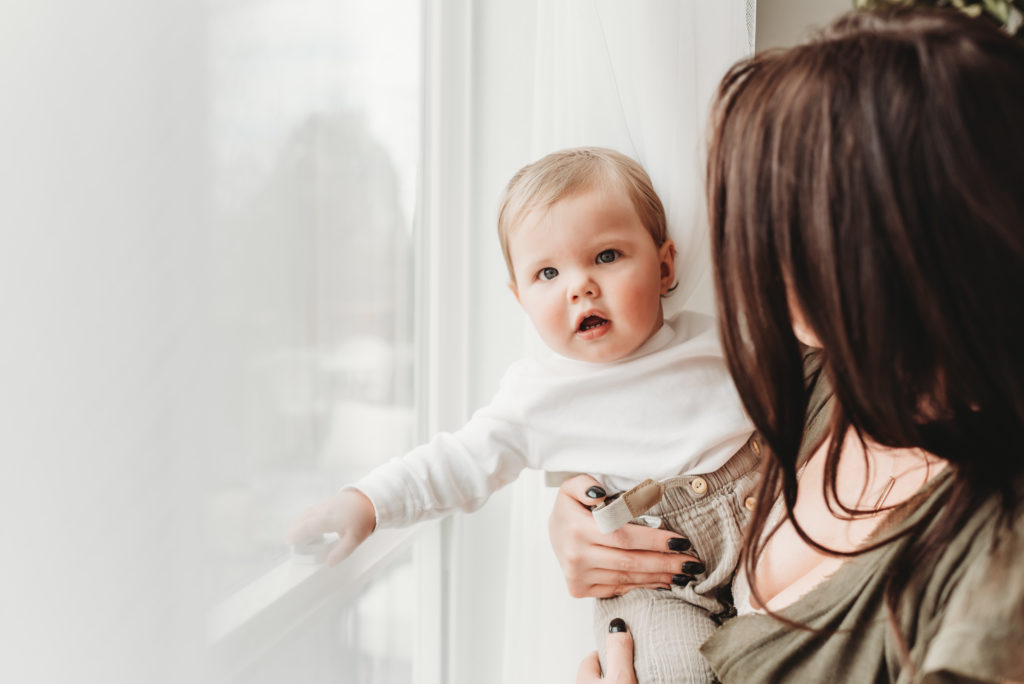 baby boy looking out the window with his mother during a motherhood photo session