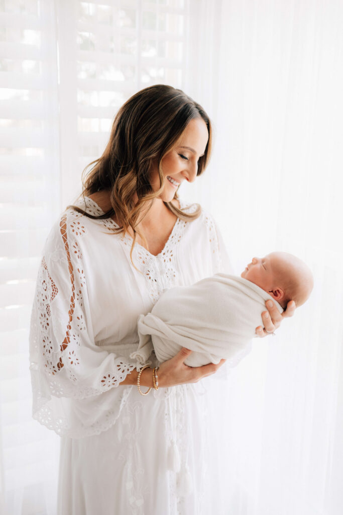 Denver photographer session with mom holding swaddled newborn in front of bright windows