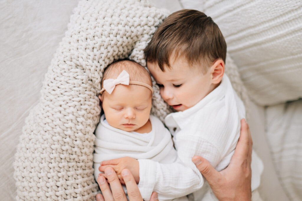 newborn baby wrapped up with toddler brother lying beside her with his hand on her