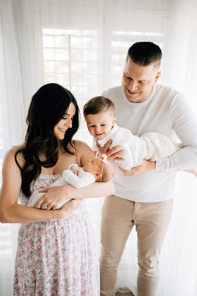 mom holding newborn baby while dad zooms toddler son toward mom and baby at denver photo session