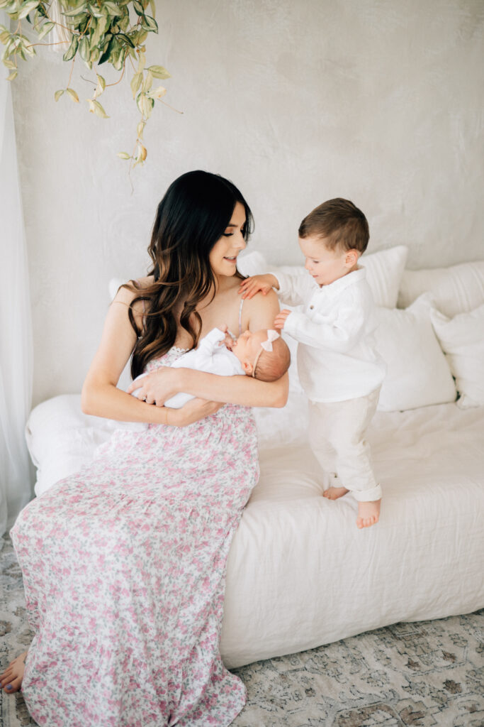 what happens when mom holds newborn on the edge of the bed while toddler son points to baby