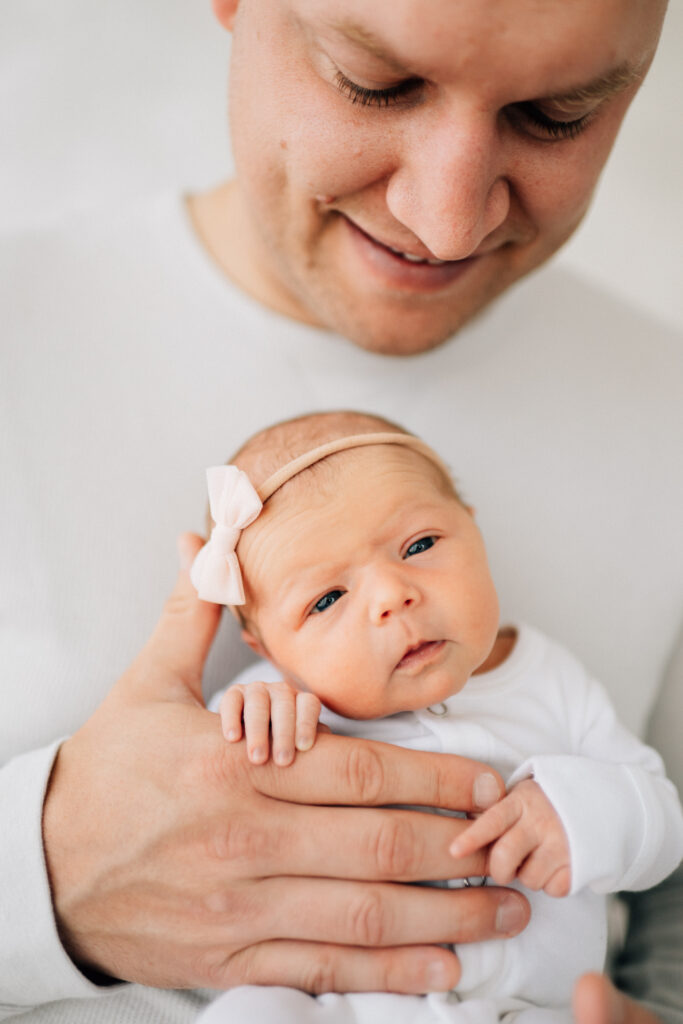 dad holding newborn daughter against his chest while she looks at the photographer