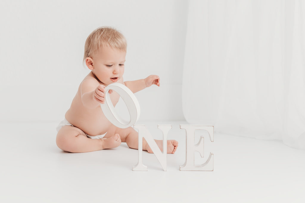 one year old baby playing with wooden letters spelling ONE