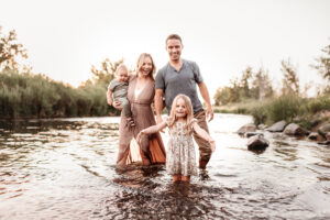 family with toddlers walking through Denver river and girl splashing water