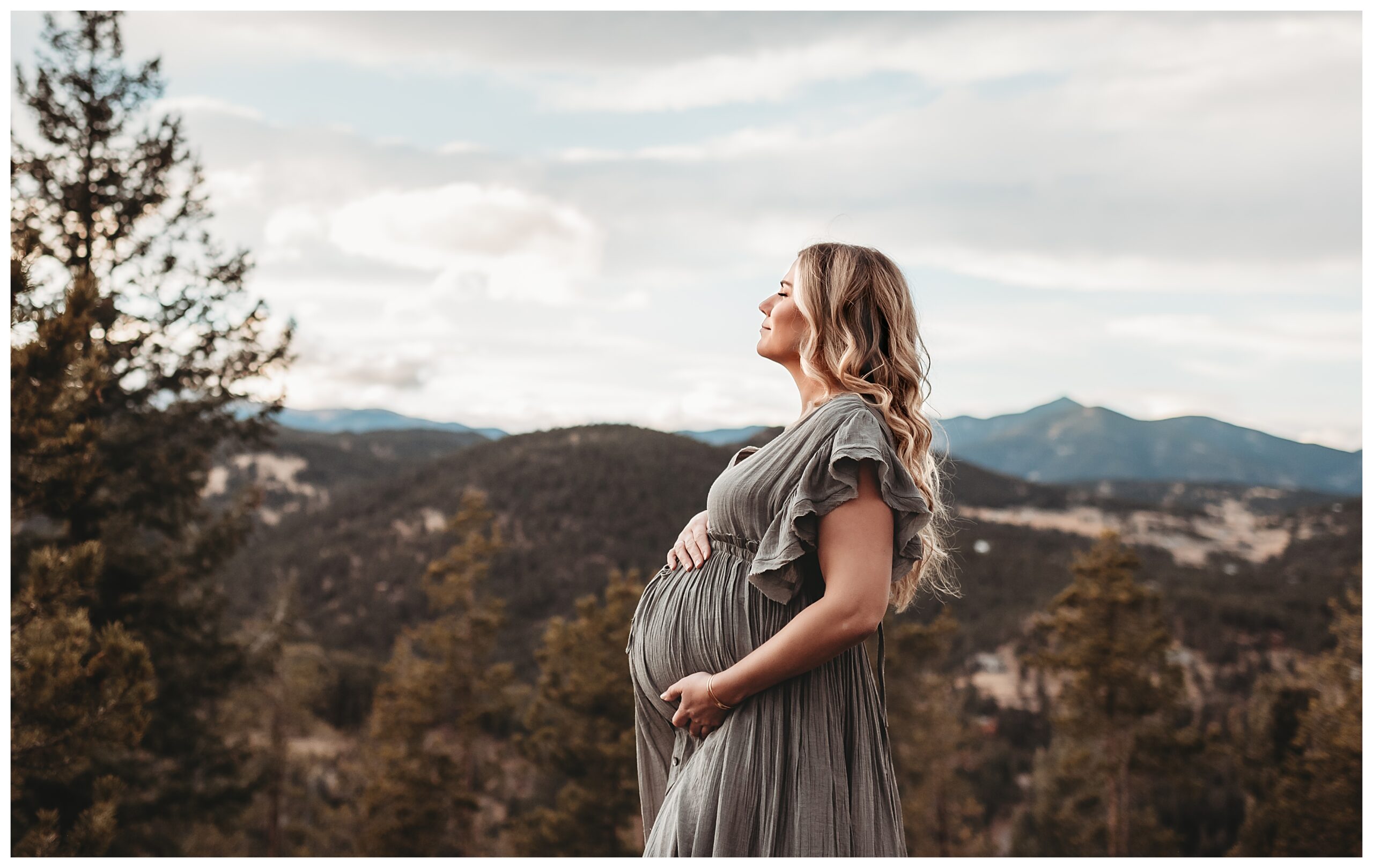 pregnant woman with hand on belly looking out at evergreen colorado