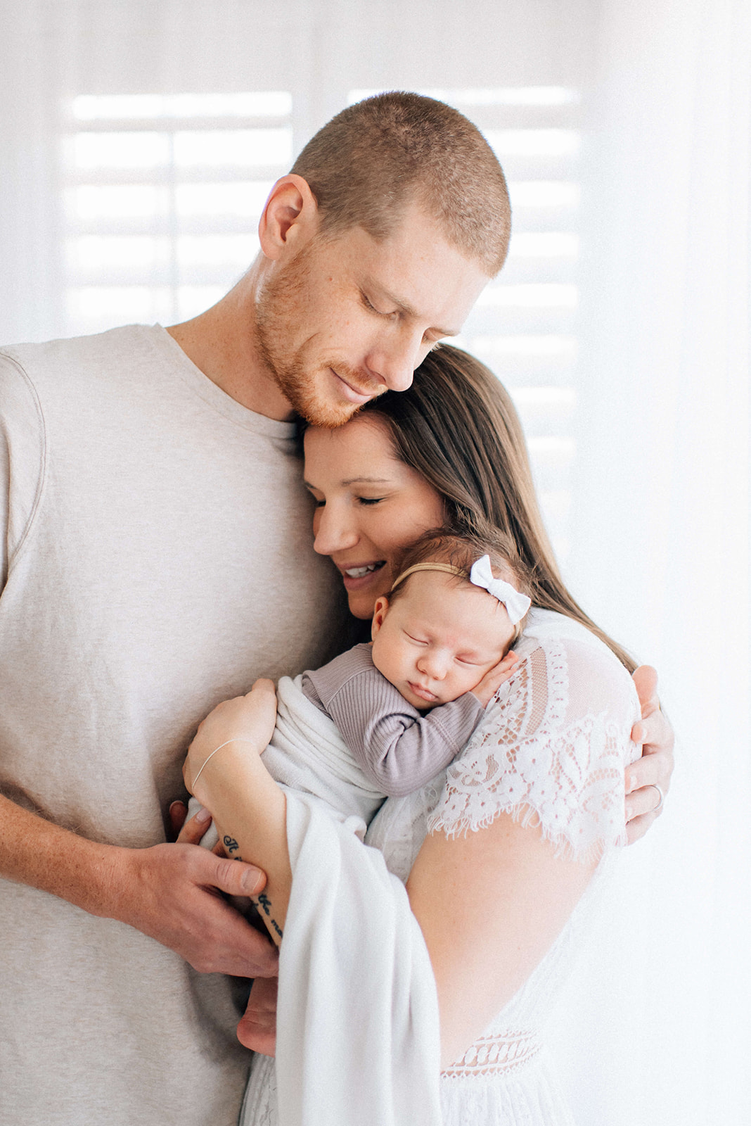Happy new mom and dad snuggle as their newborn daughter sleeps on mom's shoulder