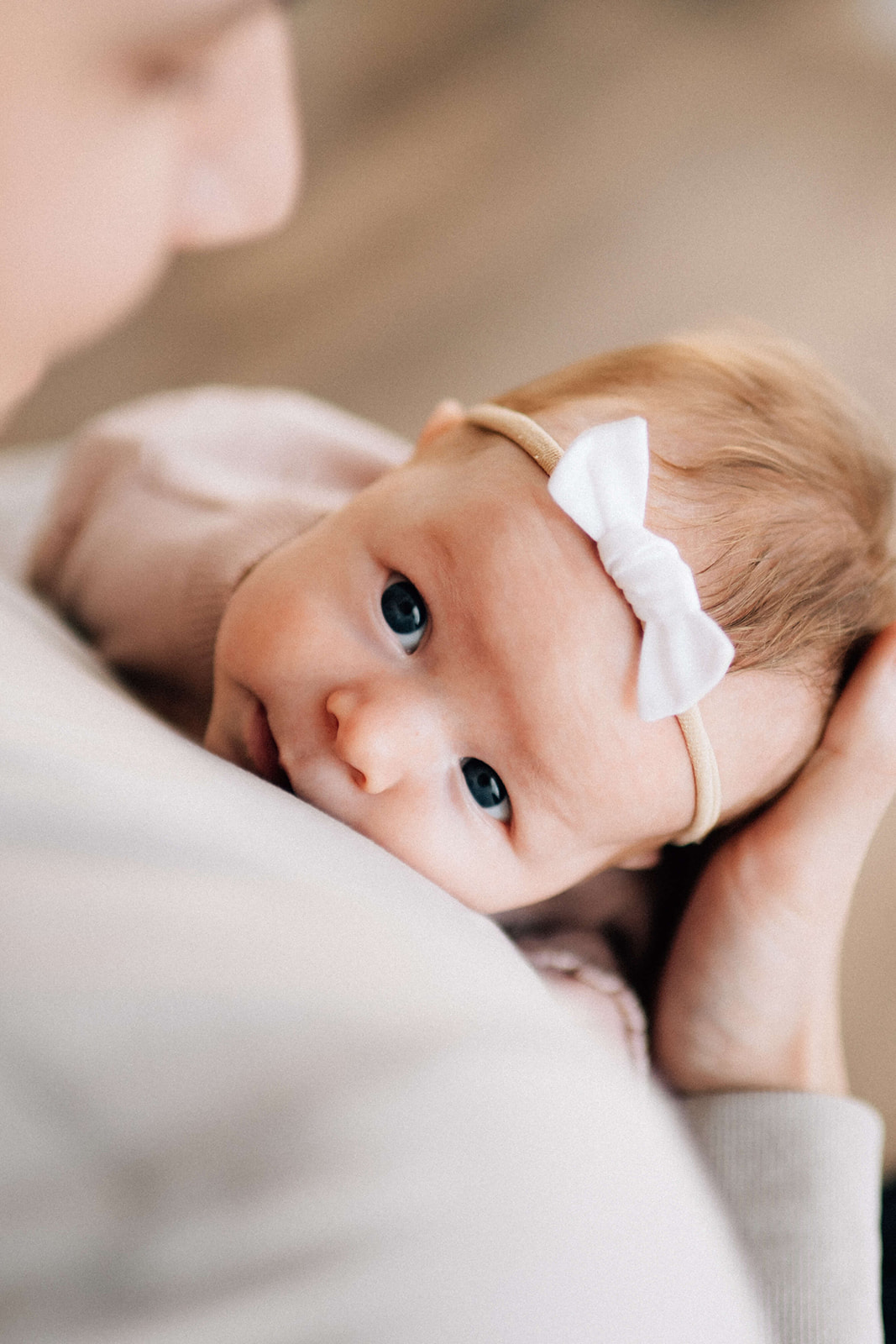 A closeup of a baby girl with eyes open laying on dad's chest with a white bow headband after visiting baby stores in Denver