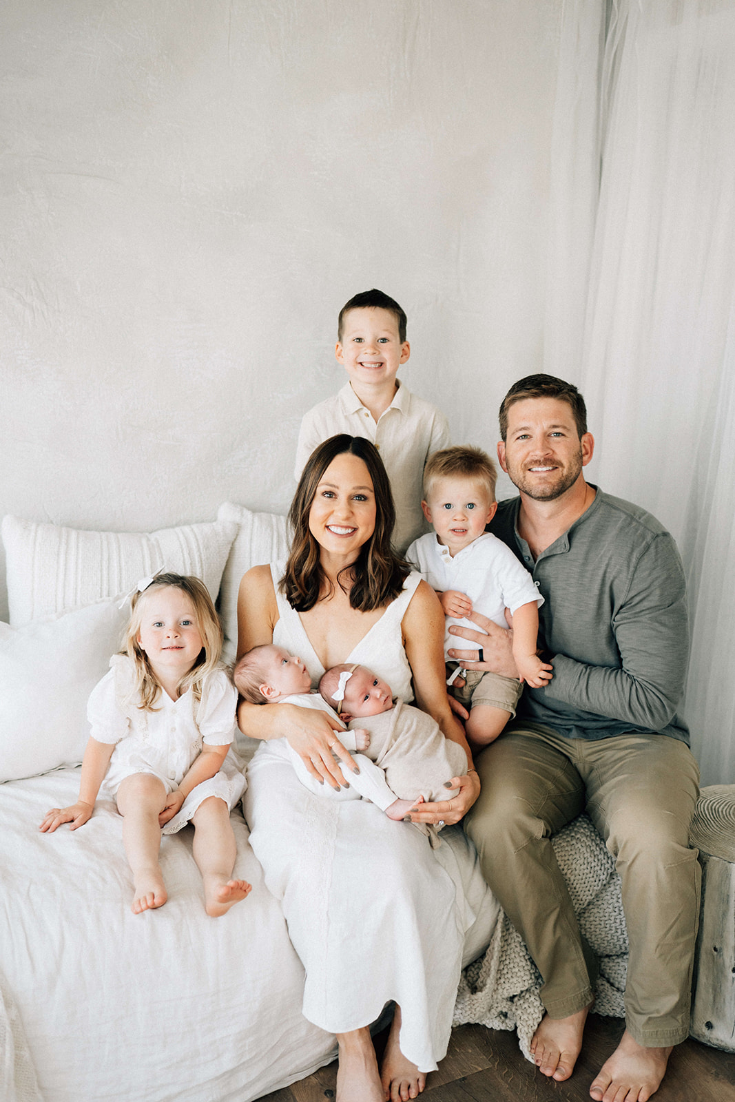 A mom and dad sit on a bed with their three toddlers and twin newborns after finding perfect nannies in Denver