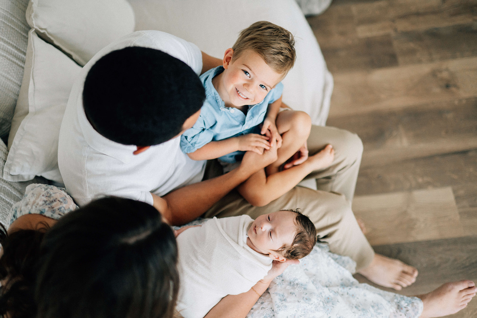 A look down over a happy family with a toddler and newborn in mom and dad's lap on a couch