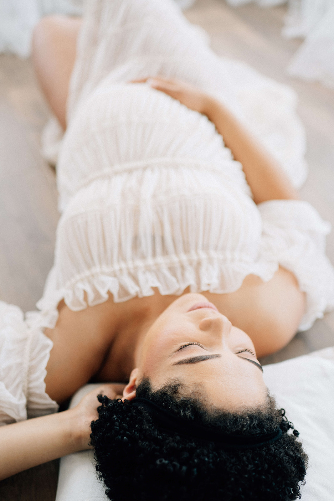 A mom to be relaxes on a cushion with a hand on her bump in a white maternity dress after a prenatal massage in Denver