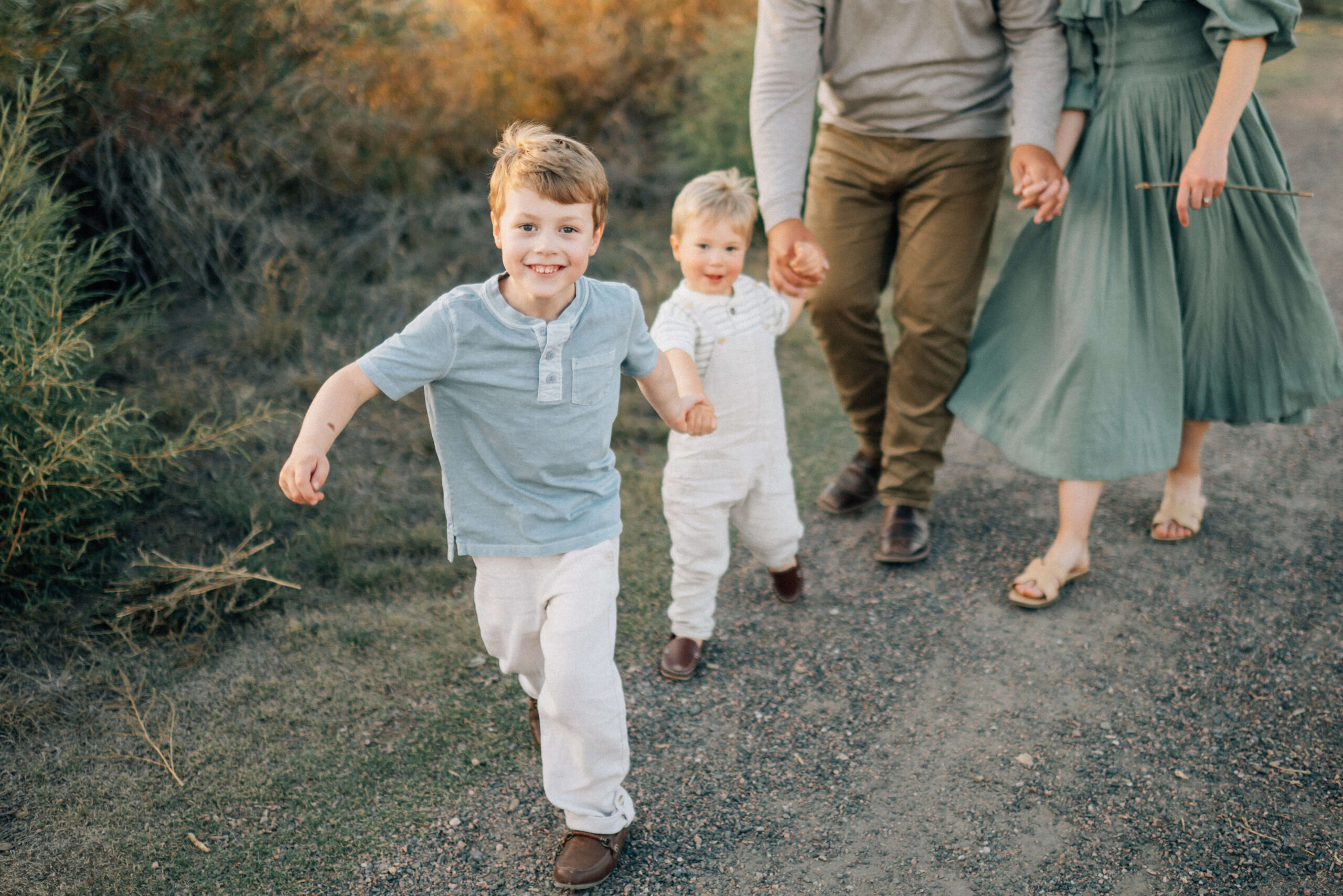 family outdoor on a path with little boy holding his brother's hand as they walk to restaurant