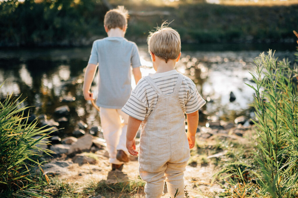 back side view of two little boys walking down to the creek with the sun shining in front of them