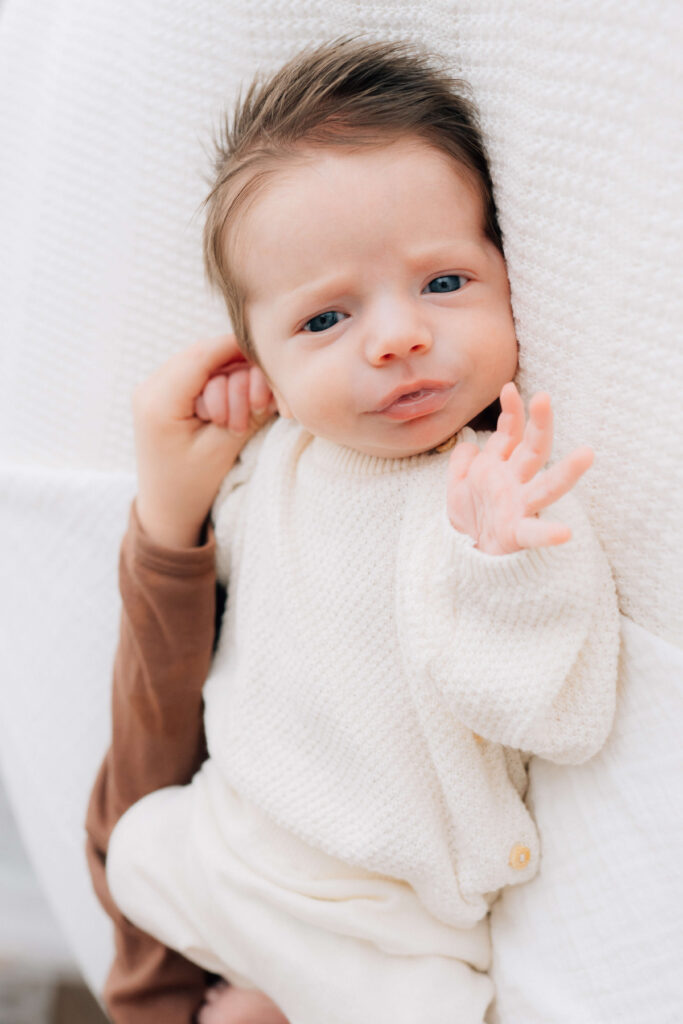 newborn baby waving to the photographer while his brother holds his other hand