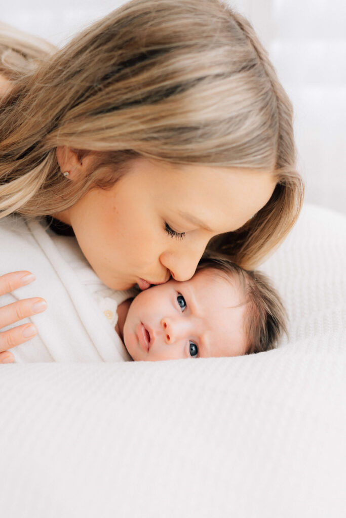 newborn baby on a blanket while his mother kisses his cheek