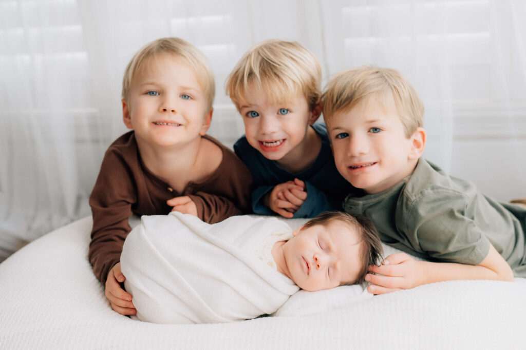 three big brothers behind their newborn baby brother in photographer studio