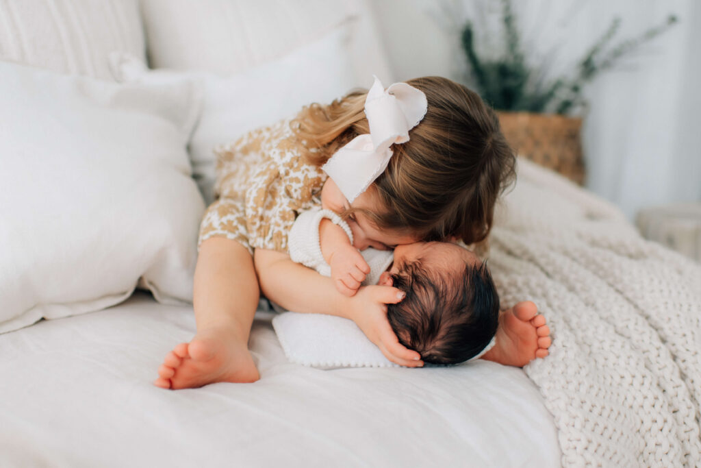 toddler girl preparing for family photos by hugging her newborn brother face to face